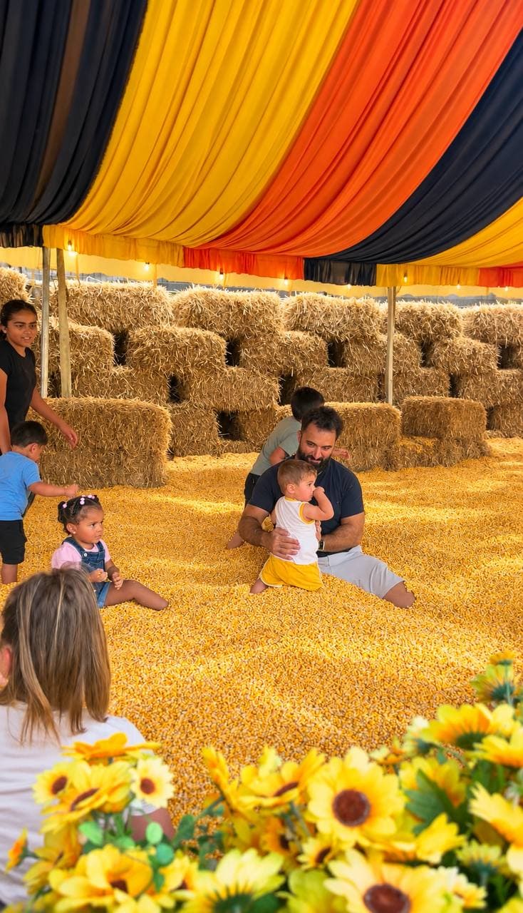 Toddlers and a parent playing in a pit of corn kernels under a striped fall tent
