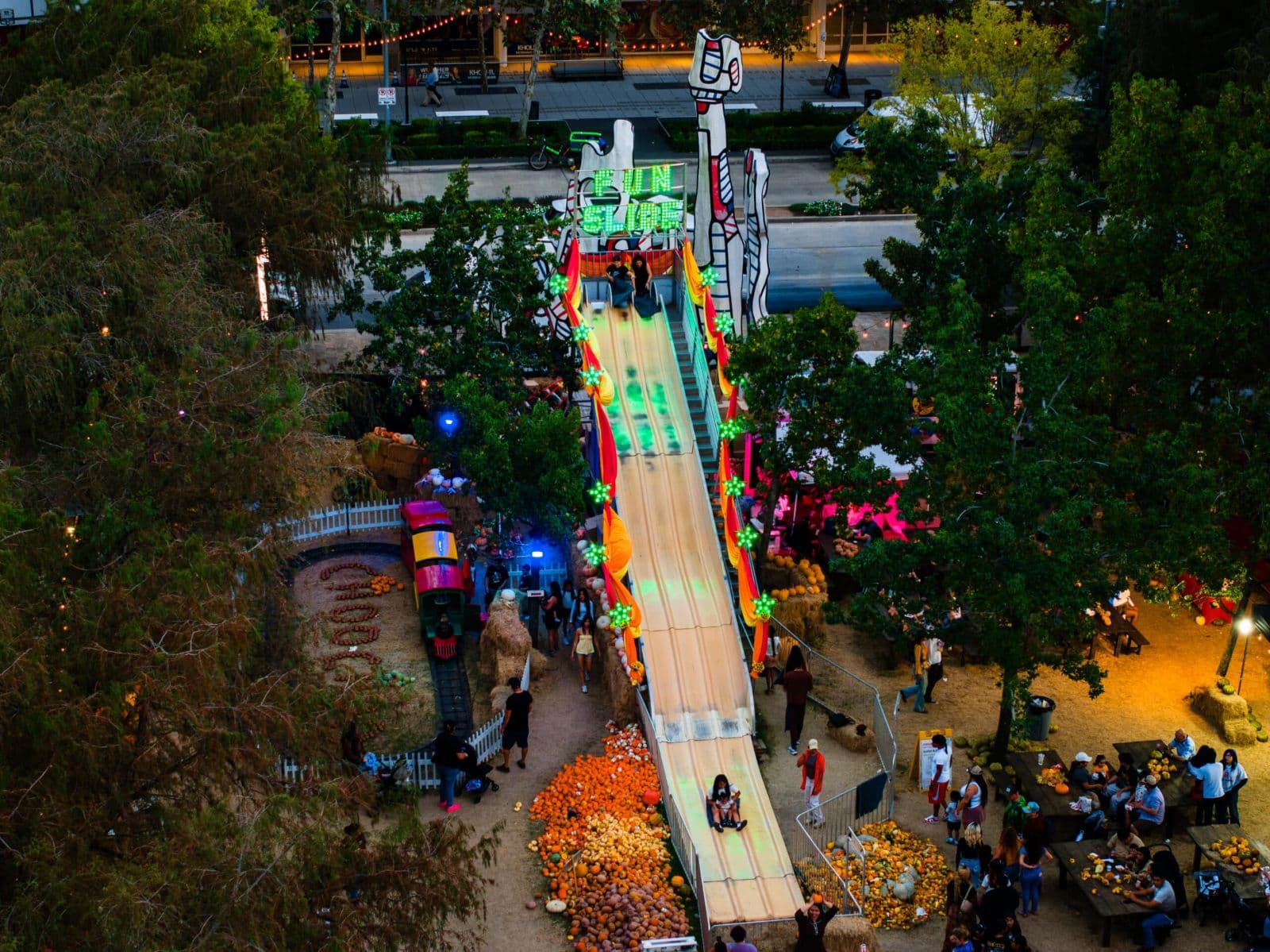 The lit 30-foot fun slide at dusk, with riders coming down past hay bales and string lights
